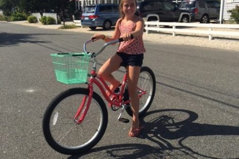 Child riding a red bicycle with a turquoise basket on a paved street.