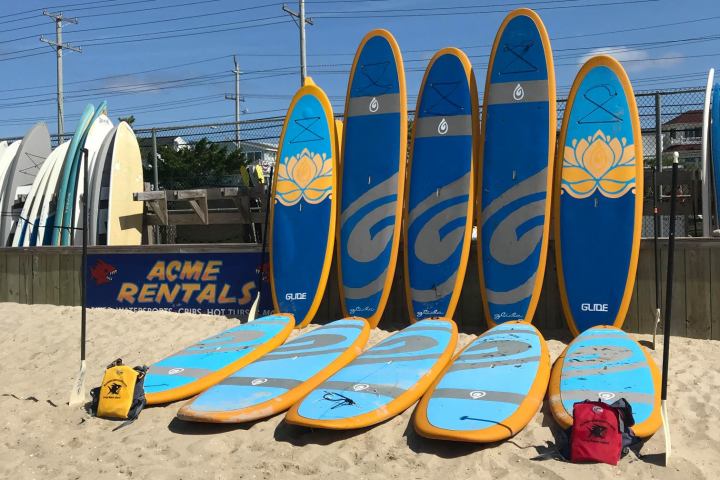 Several blue and yellow surfboards standing on a sandy beach with a sign for rentals.