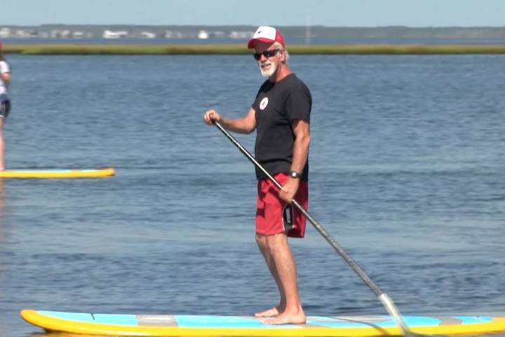 Man paddleboarding on calm water, wearing red shorts and cap.