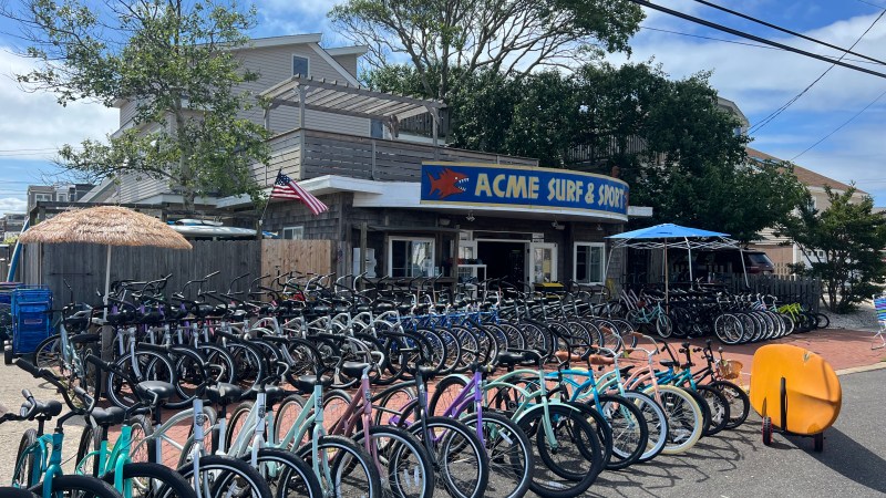 Bicycles lined up outside Acme Surf & Sport shop under a clear sky.