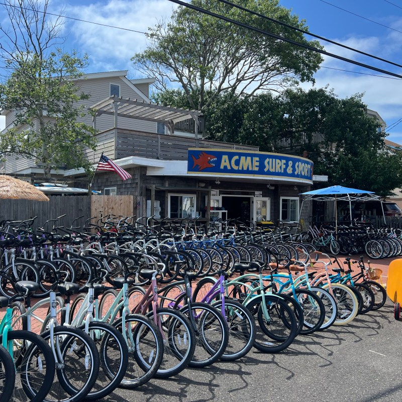 Bicycles lined up outside Acme Surf & Sport shop under a clear sky.