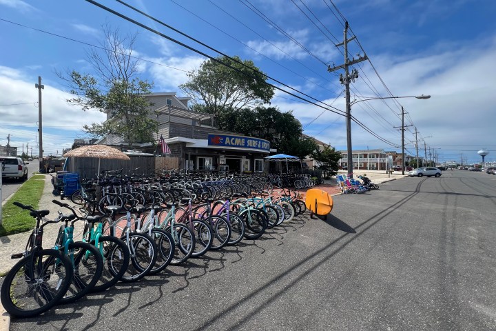 Bicycles lined up outside a surf shop under a clear blue sky on a street corner.