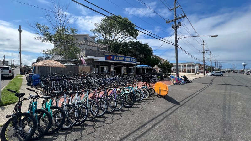 Bicycles lined up outside a surf shop under a clear blue sky on a street corner.