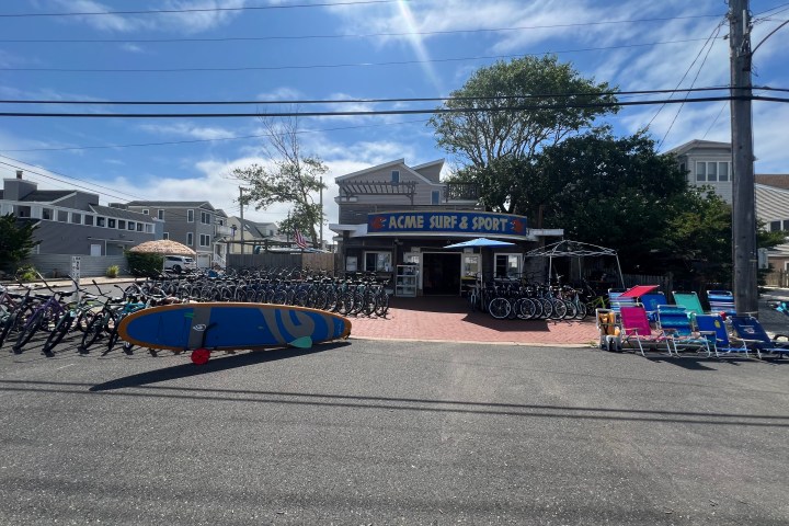 Surf shop with bicycles, surfboards, and beach chairs displayed outdoors on a sunny day.