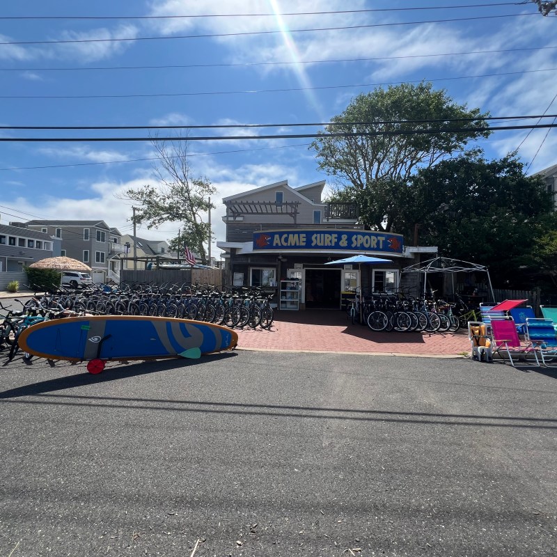 Surf shop with bicycles, surfboards, and beach chairs displayed outdoors on a sunny day.