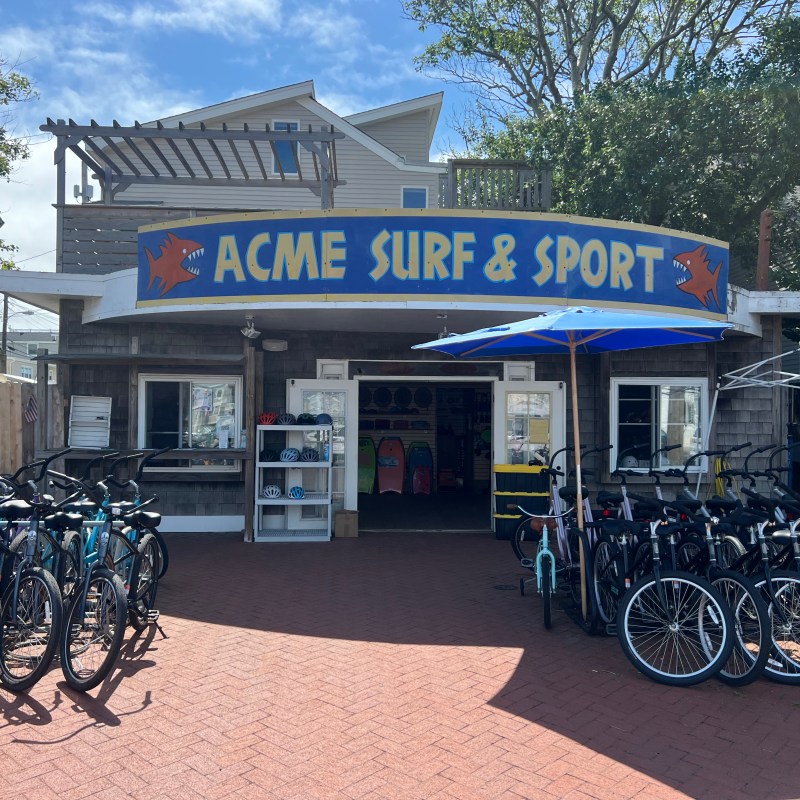 Bike rental shop with a sign reading 'Acme Surf & Sport' and bicycles outside.