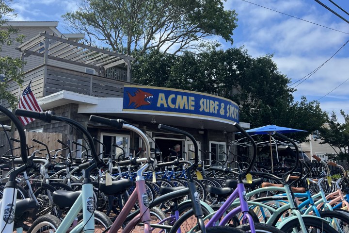 Bicycles parked in front of ACME Surf & Sport shop under a sunny sky.