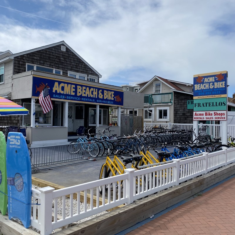 Exterior of Acme Beach & Bike shop with bikes and surfboards displayed outside.