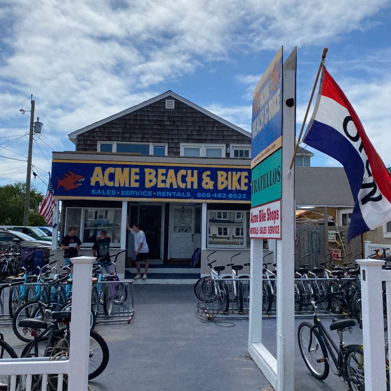 Bike shop with ACME BEACHS & BIKE sign, bikes parked outside, red and blue flags.