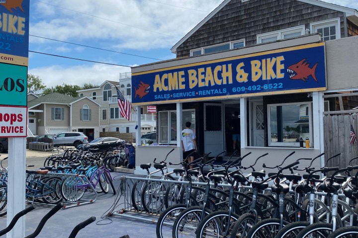 Bicycles parked in front of Acme Beach & Bike shop under a cloudy sky.
