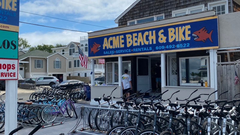 Bicycles parked in front of Acme Beach & Bike shop under a cloudy sky.