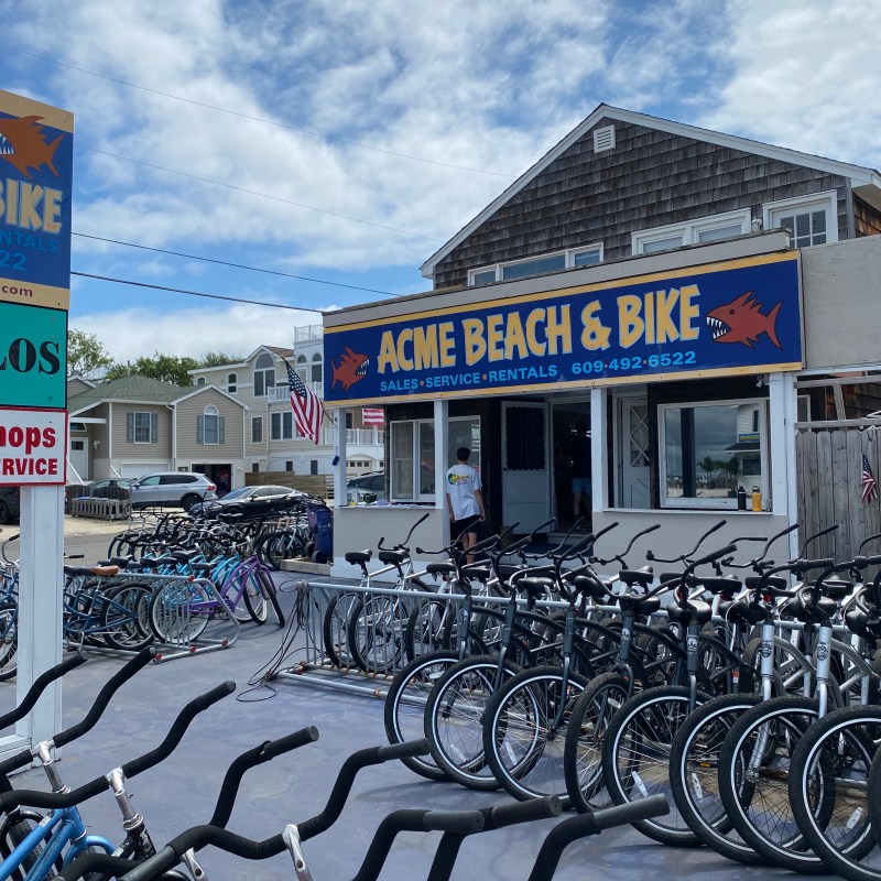 Bicycles parked in front of Acme Beach & Bike shop under a cloudy sky.