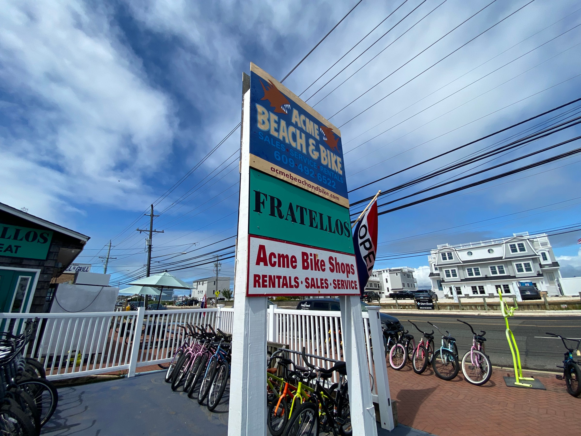 Bicycle shop with sign, rental bikes, and open flag on a sunny day.