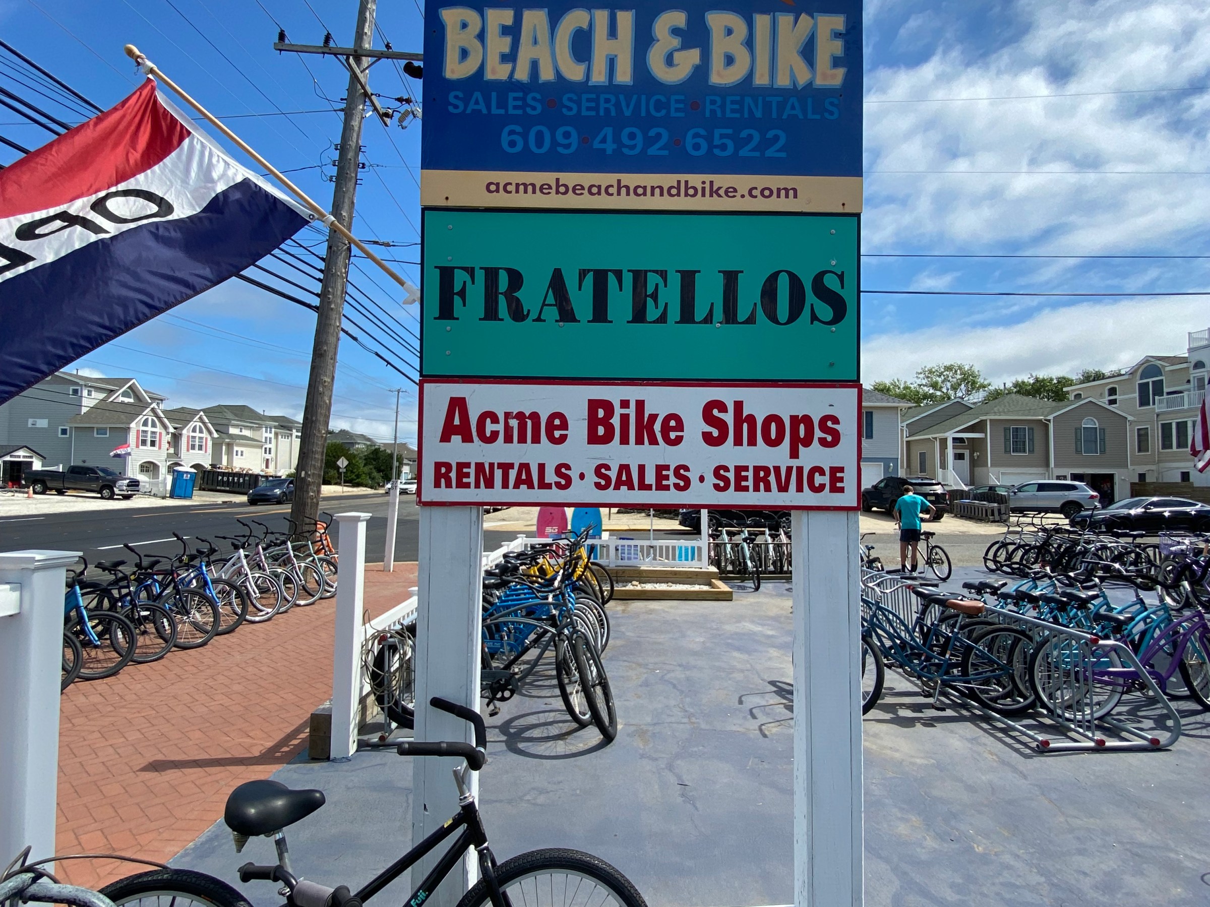 Sign for Acme Beach & Bike shop with bikes outside on a sunny day.