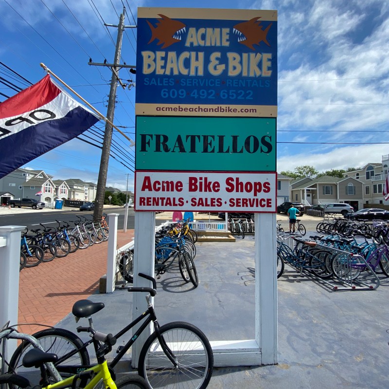 Sign for Acme Beach & Bike shop with bikes outside on a sunny day.
