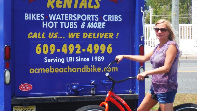 Woman with orange bike near blue rental truck with yellow text.