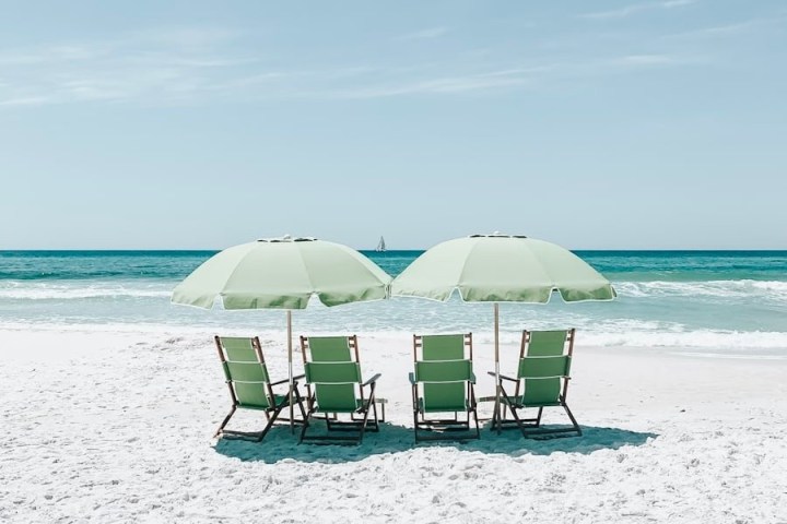 Four beach chairs under two umbrellas on a sandy beach facing the sea.